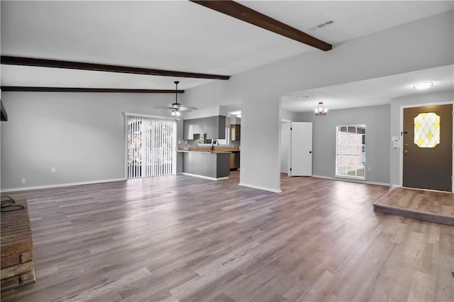 unfurnished living room with vaulted ceiling with beams, sink, ceiling fan with notable chandelier, and light wood-type flooring