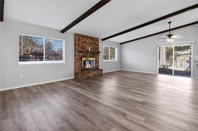 unfurnished living room featuring a fireplace, wood-type flooring, lofted ceiling with beams, and a wealth of natural light