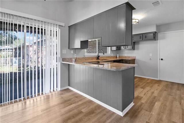 kitchen with sink, gray cabinets, light hardwood / wood-style flooring, light stone counters, and kitchen peninsula