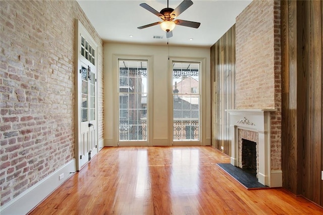 unfurnished living room with a fireplace, hardwood / wood-style flooring, ceiling fan, and brick wall