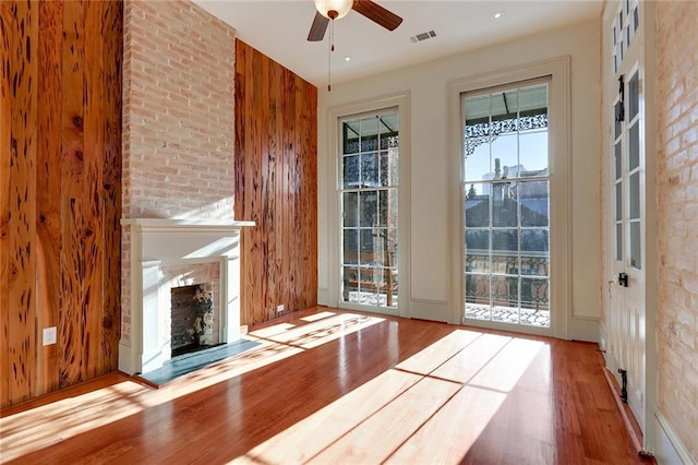 entryway with ceiling fan, light wood-type flooring, a fireplace, and wooden walls