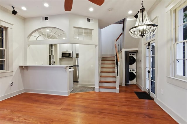 kitchen with stainless steel appliances, wood-type flooring, decorative light fixtures, stacked washer / drying machine, and white cabinets