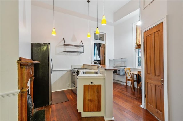 kitchen with sink, dark wood-type flooring, kitchen peninsula, pendant lighting, and appliances with stainless steel finishes