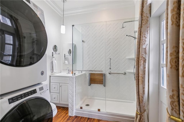 bathroom featuring vanity, a shower with door, crown molding, stacked washing maching and dryer, and wood-type flooring