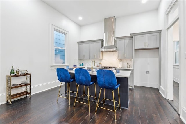 kitchen featuring a kitchen bar, gray cabinets, dark hardwood / wood-style flooring, and wall chimney range hood