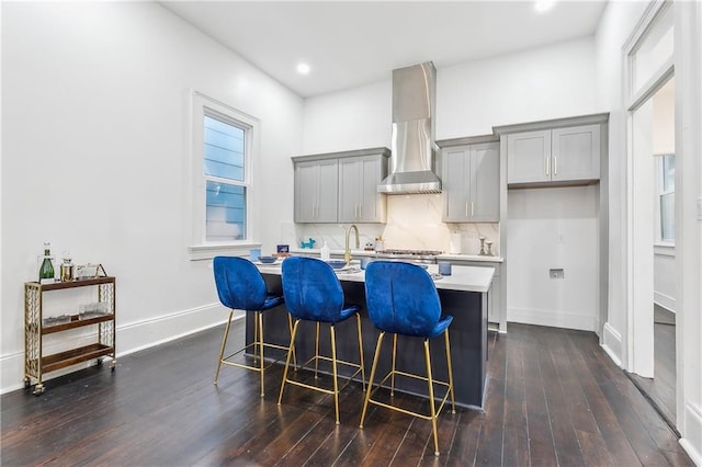 2417 Royal St, New Orleans, LA 70117 - kitchen featuring gray cabinets, an island with sink, light countertops, wall chimney range hood, and a kitchen bar