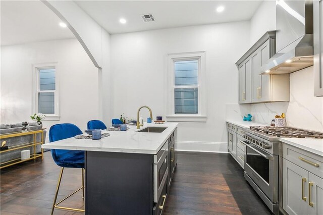 2417 Royal St, New Orleans, LA 70117 - kitchen with high end stainless steel range oven, wall chimney exhaust hood, a kitchen breakfast bar, gray cabinets, and a center island with sink