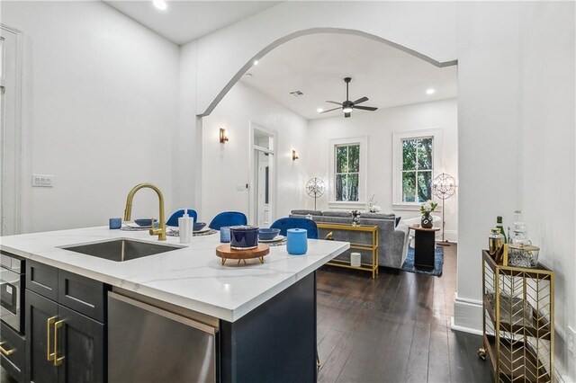 kitchen with light stone counters, ceiling fan, a kitchen island with sink, sink, and dark hardwood / wood-style floors