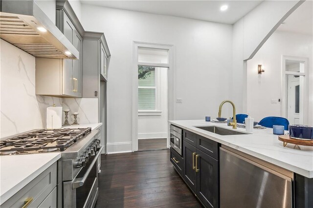 kitchen featuring appliances with stainless steel finishes, gray cabinetry, wall chimney exhaust hood, dark wood-type flooring, and sink