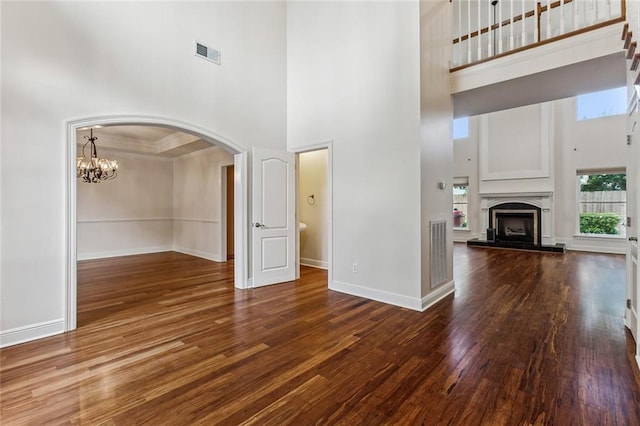 unfurnished living room with hardwood / wood-style floors, a towering ceiling, and a chandelier