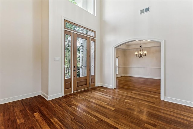 entryway with a high ceiling, dark wood-type flooring, a notable chandelier, and ornamental molding