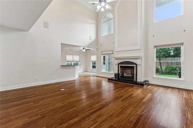 unfurnished living room featuring a tile fireplace, ceiling fan, a towering ceiling, and wood-type flooring