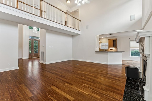 unfurnished living room with dark hardwood / wood-style flooring, plenty of natural light, a towering ceiling, and ornamental molding