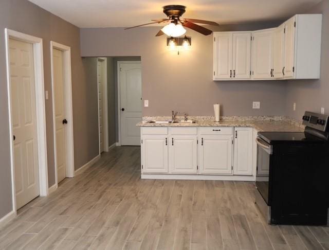 kitchen featuring stainless steel range with electric stovetop, white cabinets, light wood finished floors, and a ceiling fan