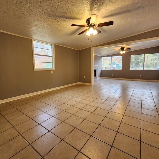 spare room featuring a ceiling fan, ornamental molding, a textured ceiling, a fireplace, and light tile patterned flooring