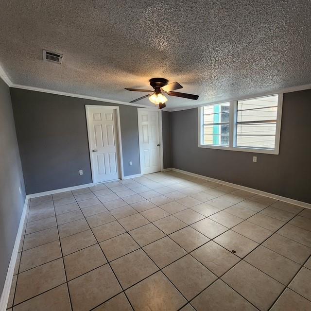 unfurnished bedroom featuring light tile patterned floors, visible vents, ornamental molding, a textured ceiling, and baseboards