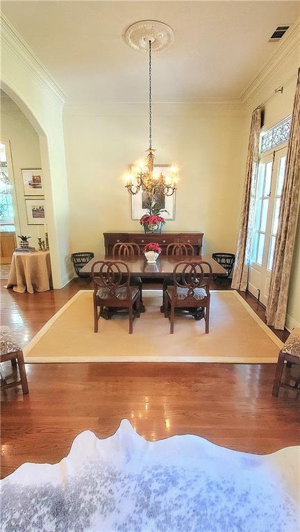 dining space featuring wood-type flooring, ornamental molding, and a notable chandelier