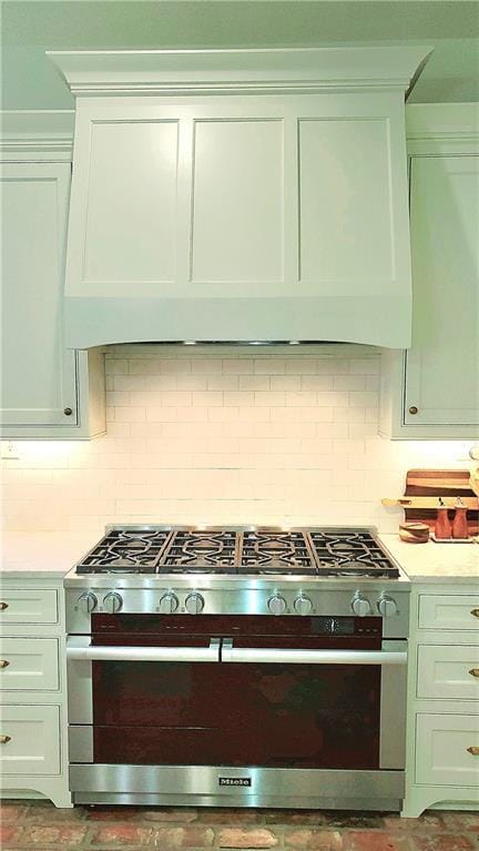 kitchen with stainless steel range, custom range hood, tasteful backsplash, and white cabinetry