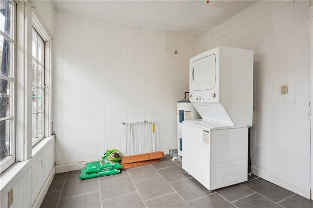 laundry room featuring stacked washer and dryer, dark tile patterned floors, wooden walls, and water heater