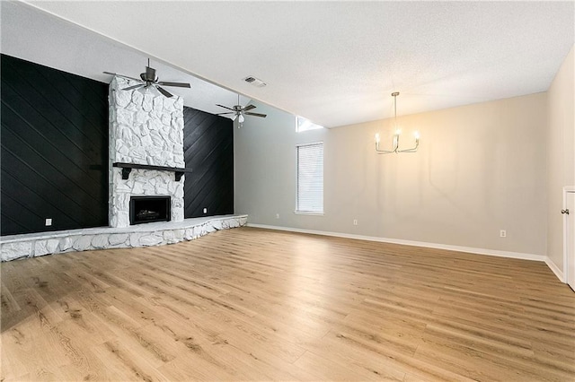 unfurnished living room featuring light wood-type flooring, a textured ceiling, vaulted ceiling, wooden walls, and a fireplace