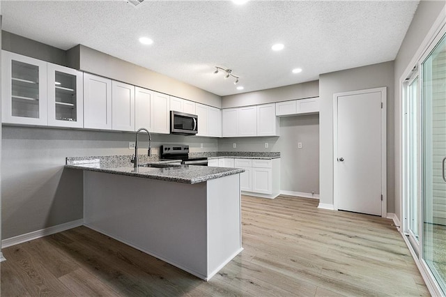 kitchen with appliances with stainless steel finishes, sink, light hardwood / wood-style flooring, dark stone countertops, and white cabinets