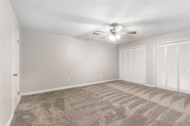 unfurnished bedroom featuring carpet, ceiling fan, a textured ceiling, and multiple closets