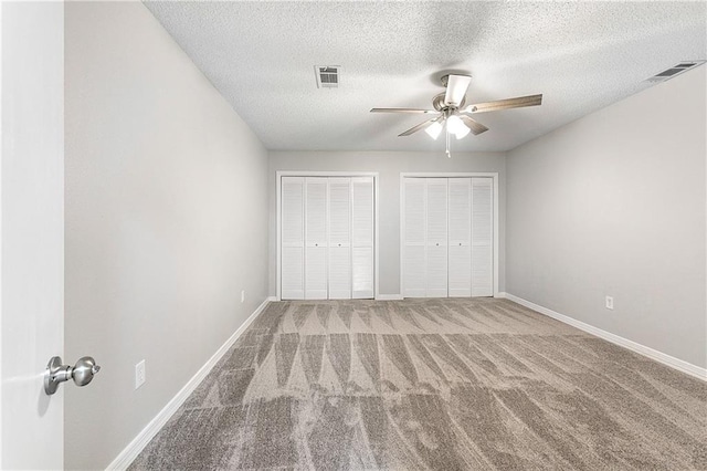 unfurnished bedroom featuring carpet, ceiling fan, a textured ceiling, and multiple closets