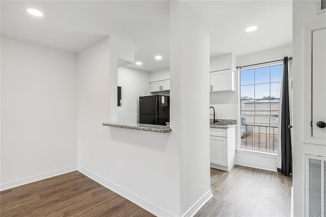 kitchen with light stone countertops, black fridge, white cabinetry, and hardwood / wood-style floors