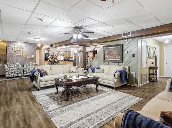 living room with wood walls, a drop ceiling, and wood-type flooring