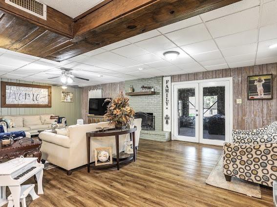 living room featuring french doors, ceiling fan, wooden walls, wood-type flooring, and a fireplace