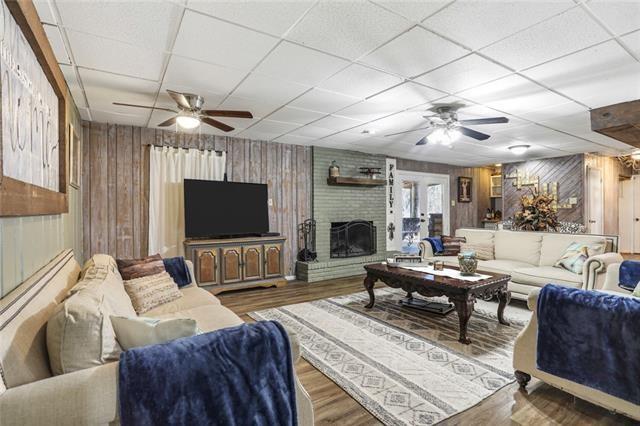 living room featuring ceiling fan, a brick fireplace, hardwood / wood-style floors, a paneled ceiling, and wooden walls