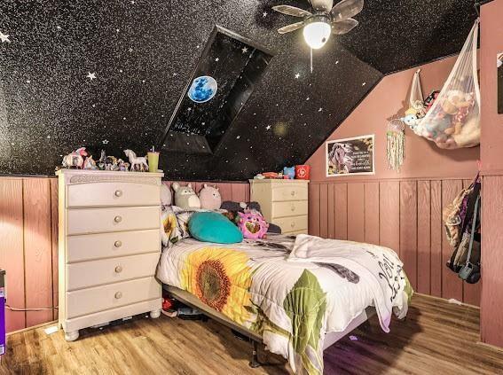 bedroom with ceiling fan, wood-type flooring, and wooden walls