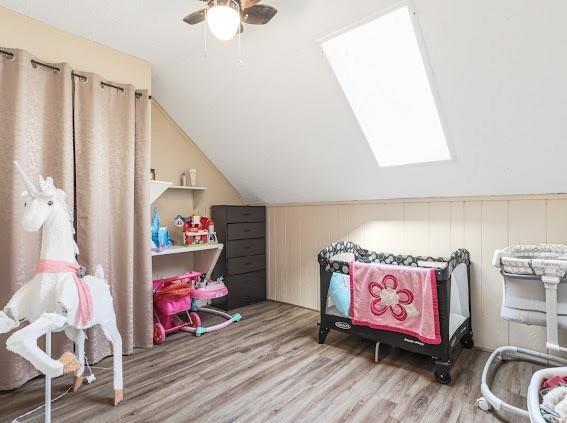 playroom with vaulted ceiling with skylight, ceiling fan, and wood-type flooring