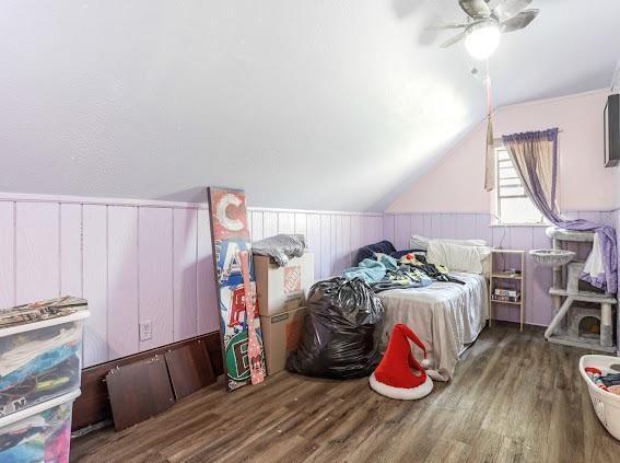 bedroom with ceiling fan, wood walls, dark hardwood / wood-style flooring, and lofted ceiling