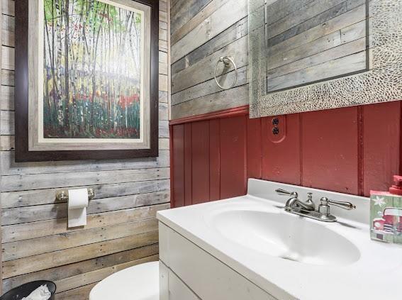 bathroom featuring vanity, wood walls, and toilet