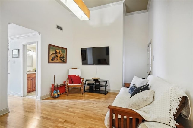 living room with a towering ceiling, light hardwood / wood-style flooring, and crown molding