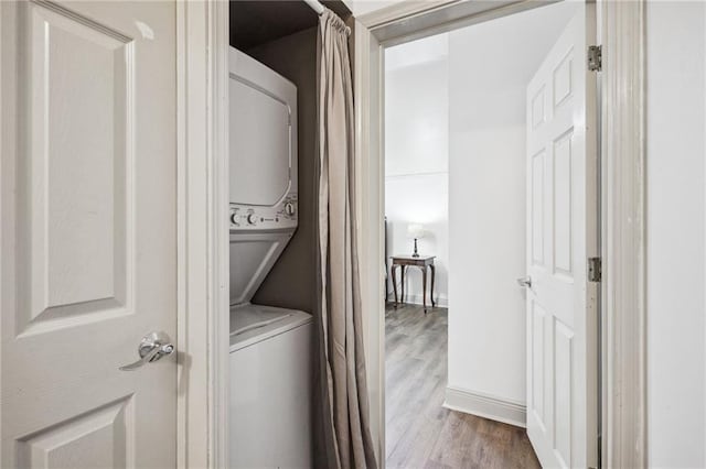 clothes washing area with baseboards, stacked washer and clothes dryer, wood finished floors, and laundry area