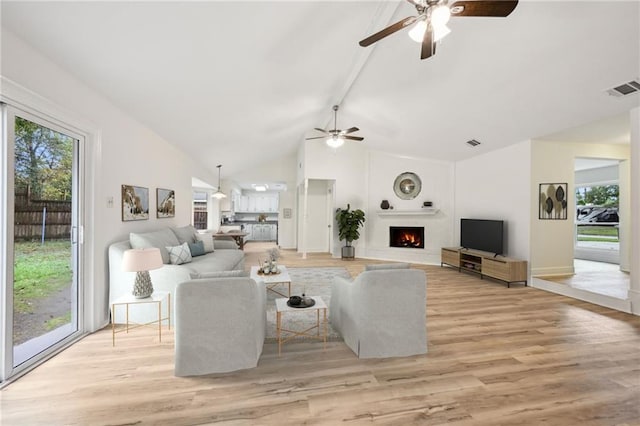 living room featuring beamed ceiling, a large fireplace, light hardwood / wood-style flooring, and a wealth of natural light