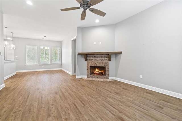 unfurnished living room featuring a fireplace, wood-type flooring, and ceiling fan with notable chandelier