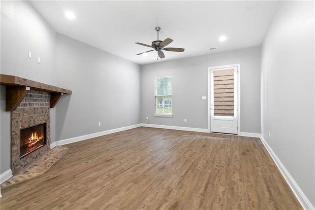 unfurnished living room featuring hardwood / wood-style floors, ceiling fan, and a brick fireplace