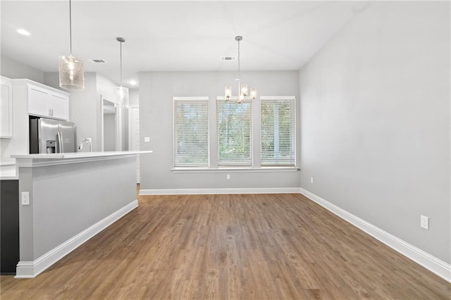 kitchen featuring stainless steel refrigerator with ice dispenser, a chandelier, pendant lighting, white cabinets, and hardwood / wood-style flooring