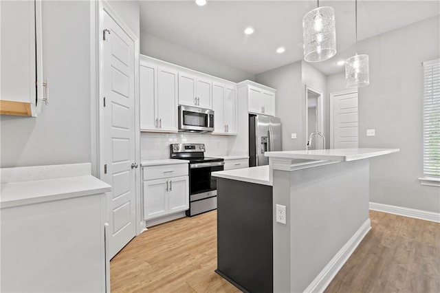 kitchen with appliances with stainless steel finishes, pendant lighting, a center island with sink, light hardwood / wood-style floors, and white cabinetry