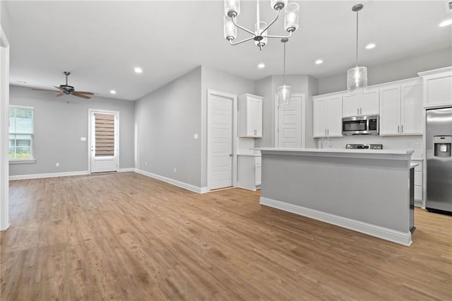 kitchen with white cabinetry, hanging light fixtures, stainless steel appliances, an island with sink, and ceiling fan with notable chandelier