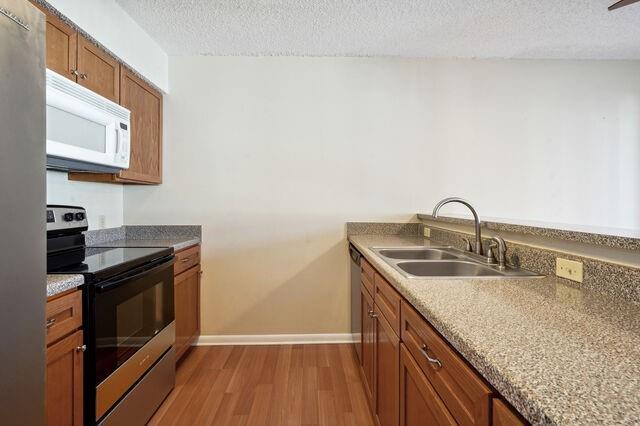 kitchen with a textured ceiling, light wood-type flooring, sink, and appliances with stainless steel finishes