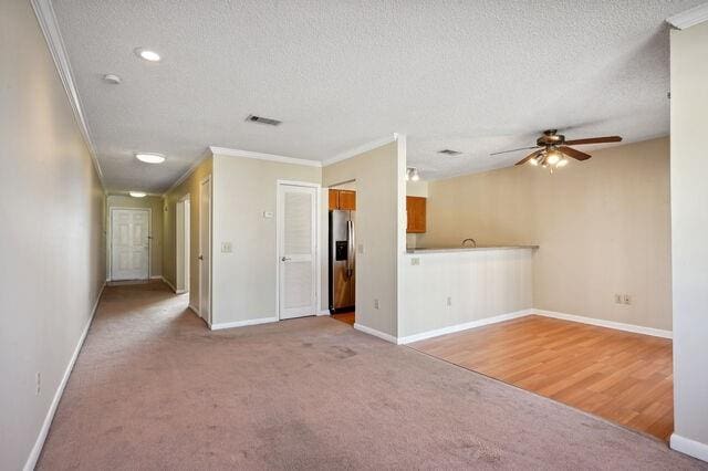 unfurnished living room featuring crown molding, ceiling fan, light carpet, and a textured ceiling