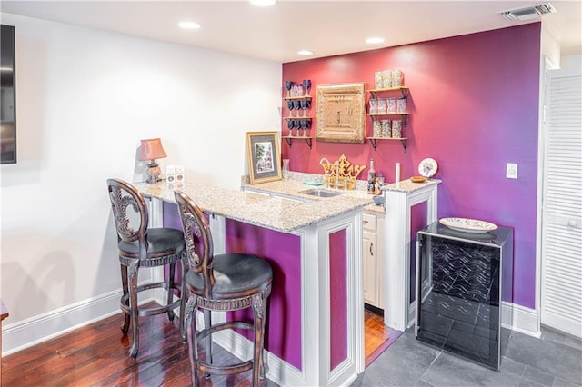 bar featuring dark hardwood / wood-style flooring, light stone counters, sink, and wine cooler