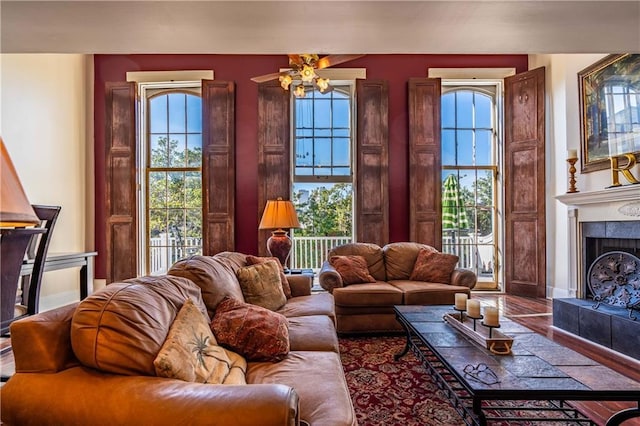 living room featuring wood-type flooring, ceiling fan, plenty of natural light, and a tiled fireplace