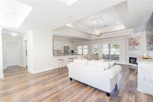 living room featuring hardwood / wood-style floors, sink, a raised ceiling, and crown molding