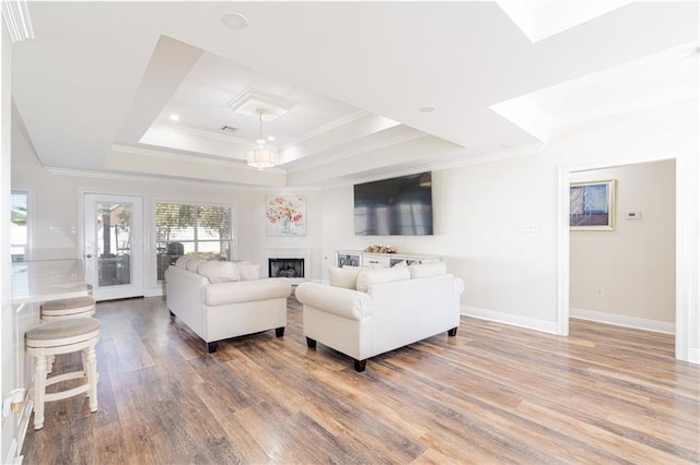 living room with hardwood / wood-style floors, a raised ceiling, and ornamental molding