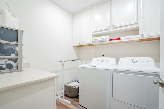 clothes washing area featuring washer and clothes dryer, cabinets, and hardwood / wood-style flooring